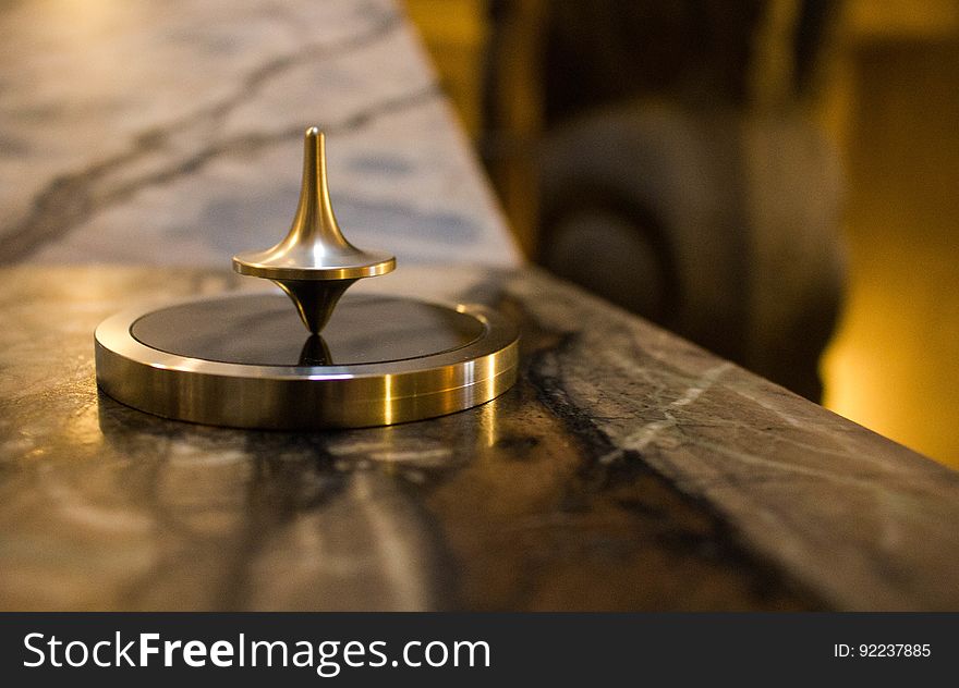 Brass top spinning on a circular wooden block surrounded by a circular brass collar place on a wooden table with selective focus, blurred background. Brass top spinning on a circular wooden block surrounded by a circular brass collar place on a wooden table with selective focus, blurred background.
