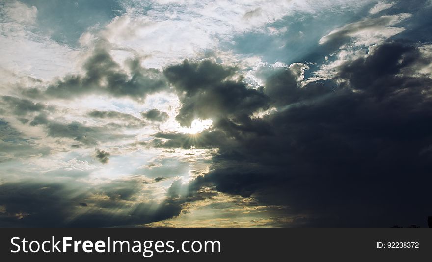 Sun with rays streaming through light and darkened storm clouds in the sky. Sun with rays streaming through light and darkened storm clouds in the sky.