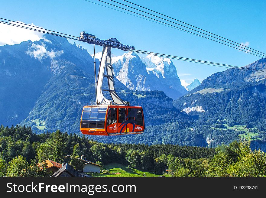 Red cable car traveling over mainly forested countryside into the snow covered mountains carrying skiers and or climbers, mountain background with blue sky. Red cable car traveling over mainly forested countryside into the snow covered mountains carrying skiers and or climbers, mountain background with blue sky.