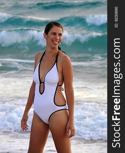 Young woman in white bathing suit standing on beach with waves in background. Young woman in white bathing suit standing on beach with waves in background