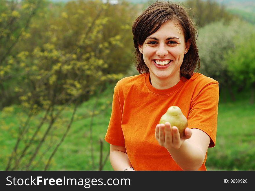 Pretty girl in orange shirt holding a pear in hand. Pretty girl in orange shirt holding a pear in hand