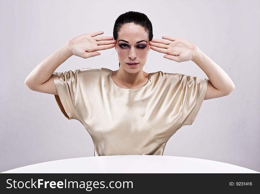 Brunette woman wearing gold shirt holding her heads up to her head. Brunette woman wearing gold shirt holding her heads up to her head