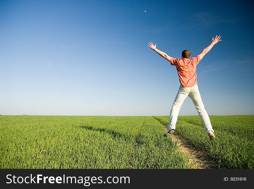 Young man jumping on green grass - arms outstretched