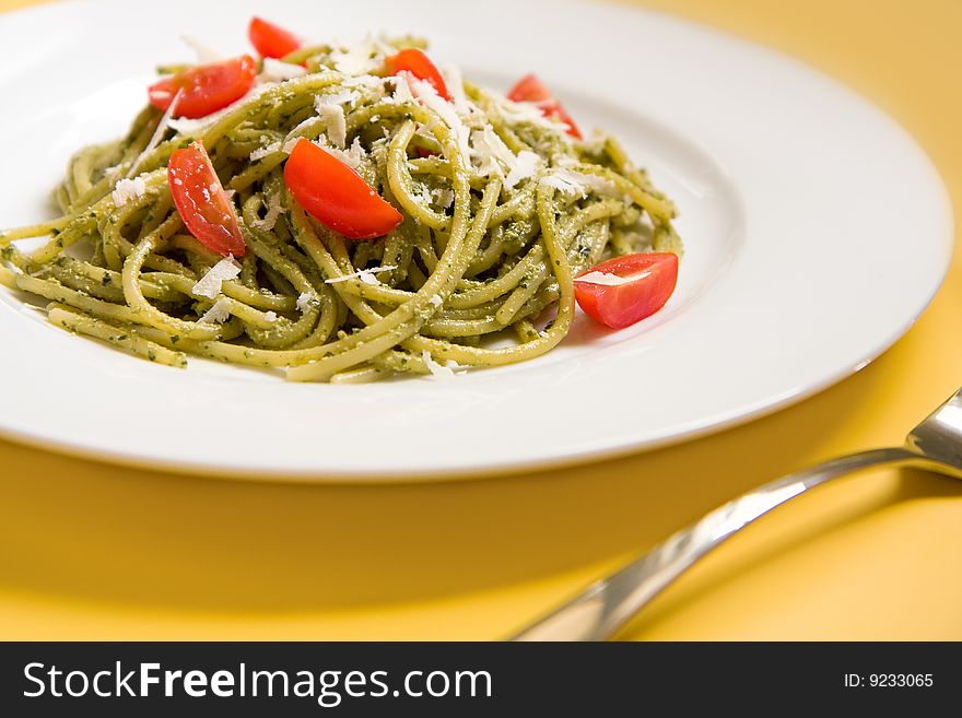 Spaghetti with basil pesto, tomatoes, and parmigiano reggiano on a white plate. Spaghetti with basil pesto, tomatoes, and parmigiano reggiano on a white plate
