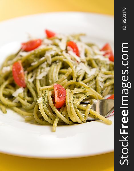 Spaghetti with basil pesto, tomatoes, and parmigiano reggiano on a white plate. Spaghetti with basil pesto, tomatoes, and parmigiano reggiano on a white plate