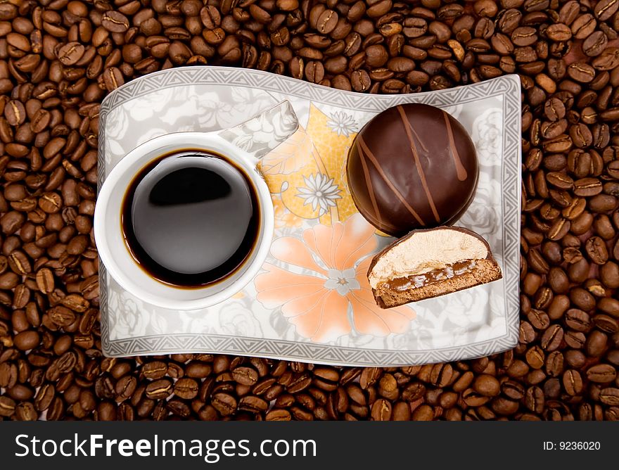 Coffee cup with sweets on beans background, high angle view