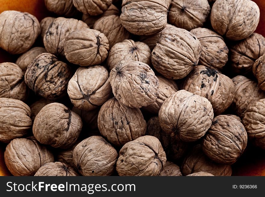 Pile of walnuts in their shells in a orange ceramic bowl