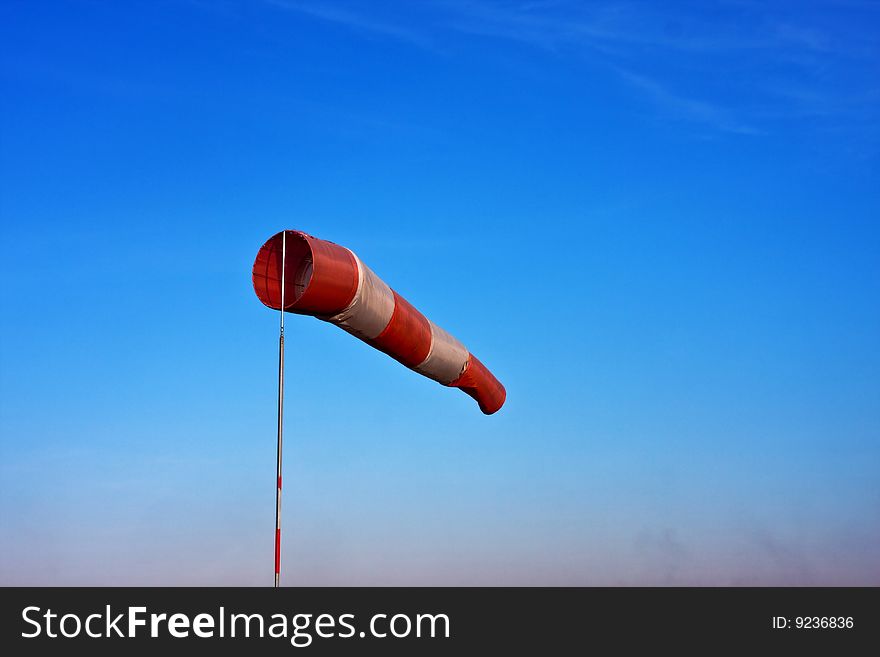 Windsock in airfield showing wind strength on blue sky background.