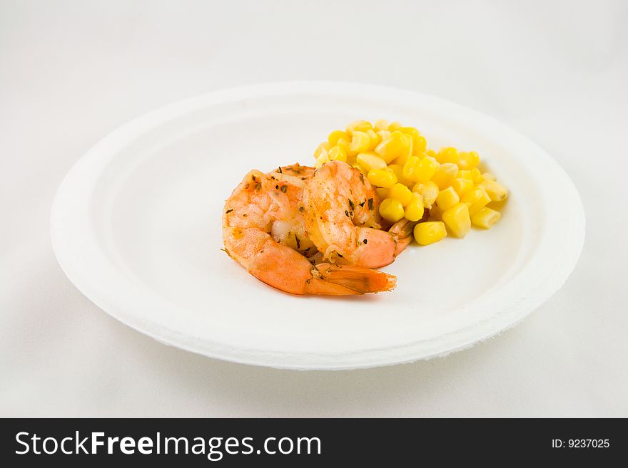 Spicy king prawns with yellow sweetcorn on a white plate on a white background. Spicy king prawns with yellow sweetcorn on a white plate on a white background