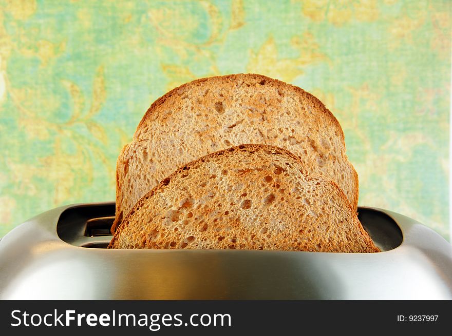 Toasted bread in a stainless steel toaster with a green background. Toasted bread in a stainless steel toaster with a green background.