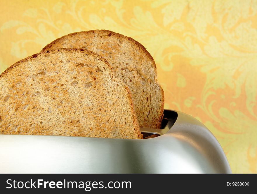 Toasted bread in a stainless steel toaster with a yellow background. Toasted bread in a stainless steel toaster with a yellow background.