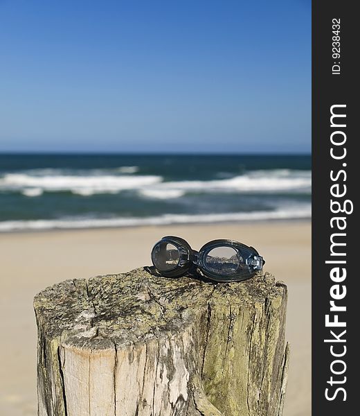 A pair of goggles sitting over a log in the beach.