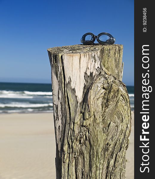 A pair of goggles sitting over a log in the beach.