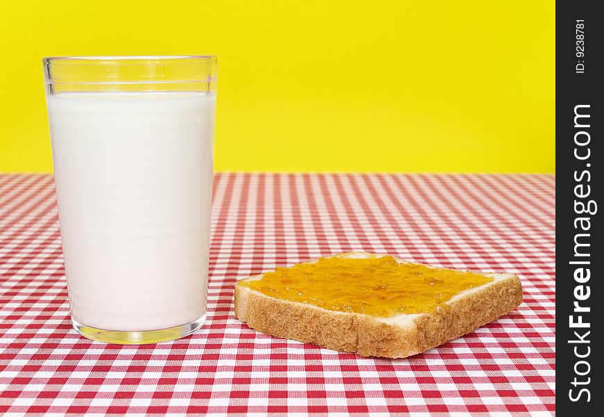 A glass of milk and a toast spread with jam over the table. A glass of milk and a toast spread with jam over the table.