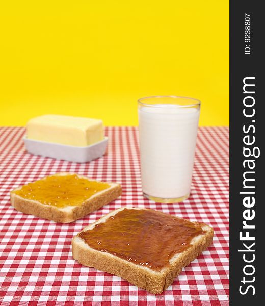 Two slices of bread spread with jam, a glass of milk and a butter stick. Two slices of bread spread with jam, a glass of milk and a butter stick.