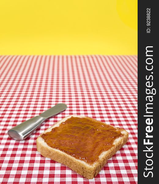 A slice of bread spread with jam and a knife over the table. A slice of bread spread with jam and a knife over the table.