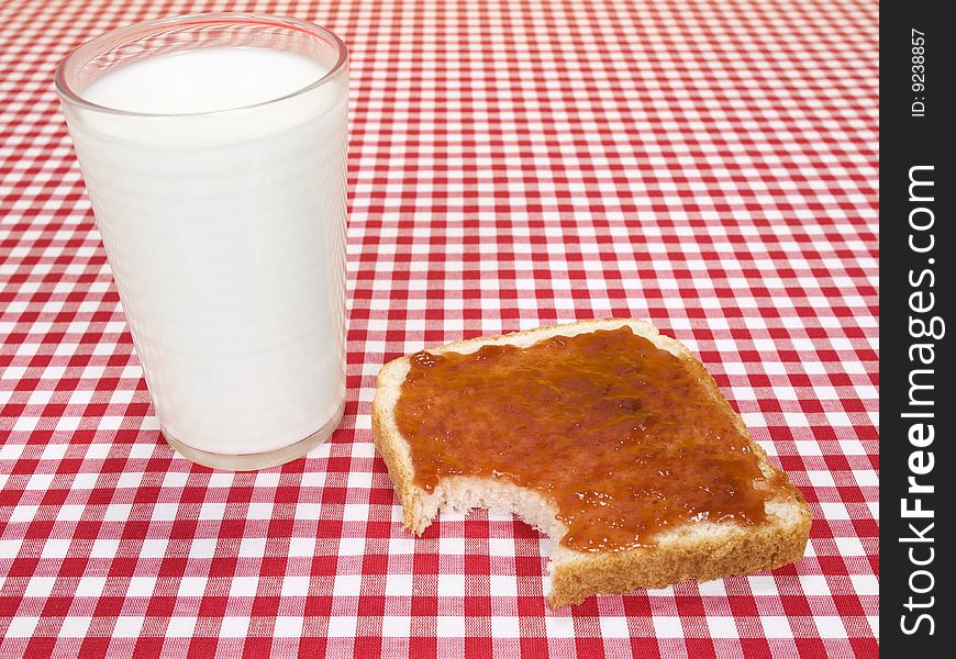 A glass of milk and a toast spread with jam, with a bite missing. A glass of milk and a toast spread with jam, with a bite missing.