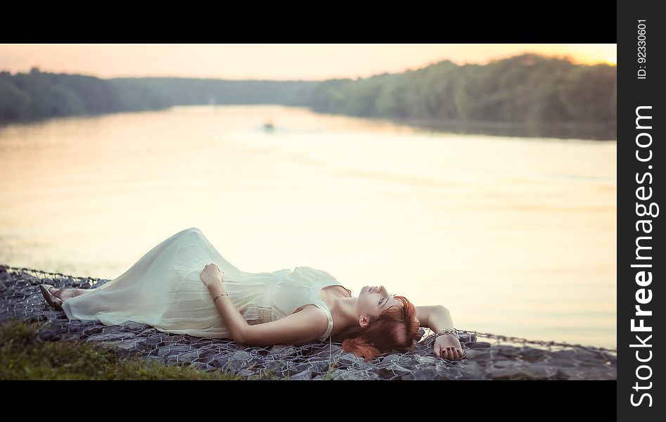 A woman in long dress lying on a shore of a river or a lake. A woman in long dress lying on a shore of a river or a lake.
