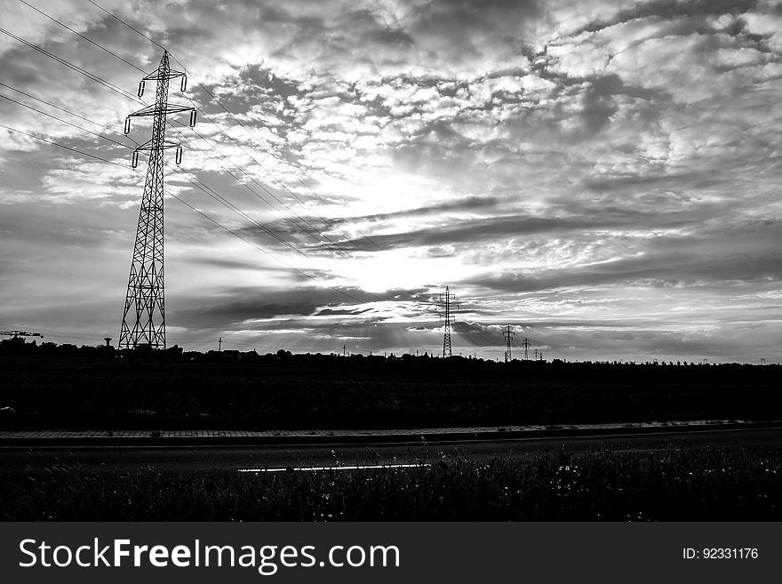 Electricity pylons stretching into the distance in a dark landscape at dawn fluffy gray clouds. Electricity pylons stretching into the distance in a dark landscape at dawn fluffy gray clouds.