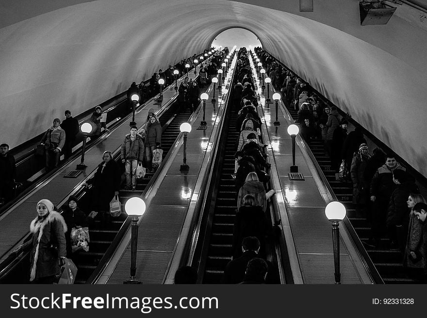 A view in a subway escalator with commuters on and other passengers in black and white. A view in a subway escalator with commuters on and other passengers in black and white.