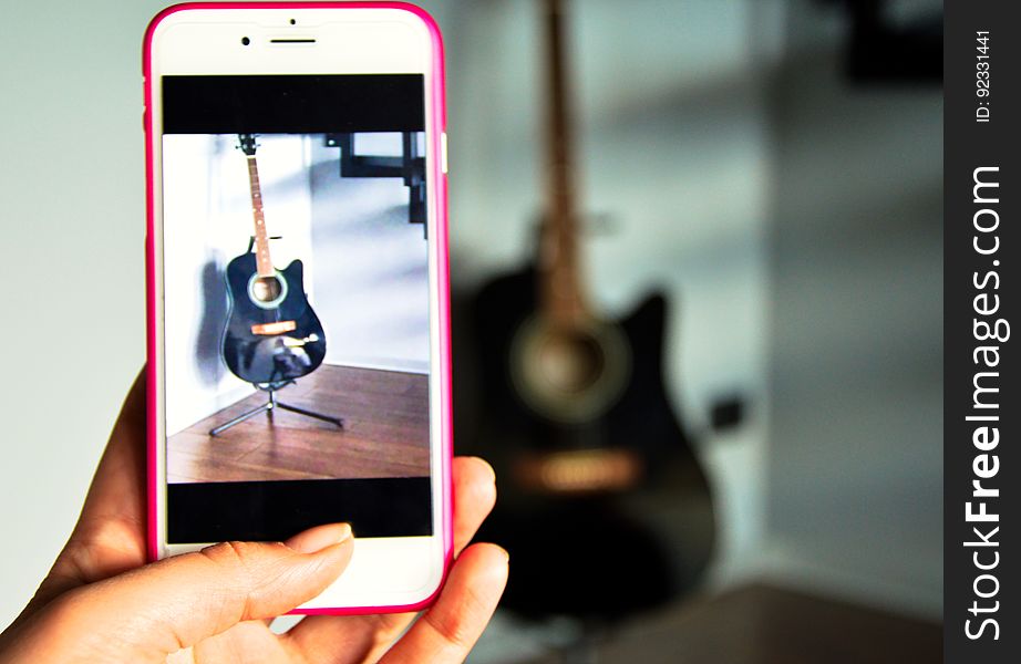 A person taking a photo of a guitar with a mobile phone. A person taking a photo of a guitar with a mobile phone.