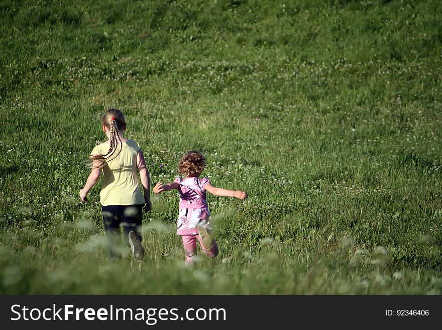 Two cute little girls walking on the lawn at summer