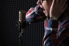 Close-up Portrait Of A Young Guy Lip Singing Emotionally In Front Of A Microphone And Holding Hands On Headphones. Royalty Free Stock Photography