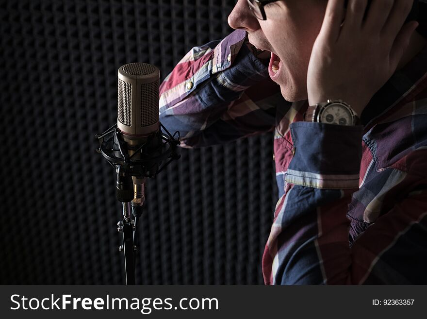 Close-up Portrait Of A Young Guy Lip Singing Emotionally In Front Of A Microphone And Holding Hands On Headphones.