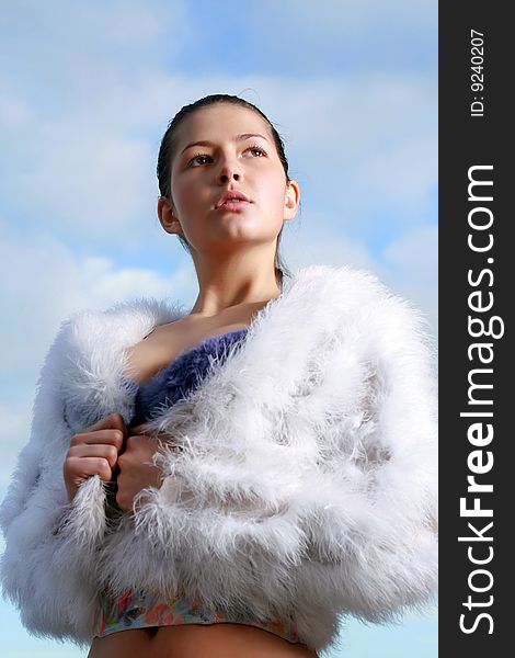 Portrait of the beautiful young woman in white fur against the blue clear sky. Portrait of the beautiful young woman in white fur against the blue clear sky