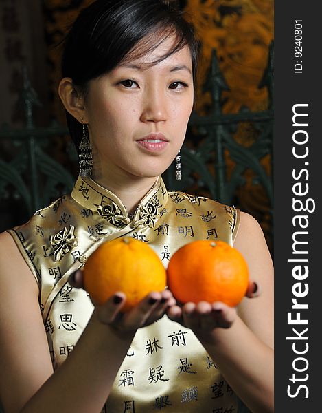 Beautiful Asian woman in cheongsam holding two oranges, suitable for Chinese New Year occasion. Beautiful Asian woman in cheongsam holding two oranges, suitable for Chinese New Year occasion.