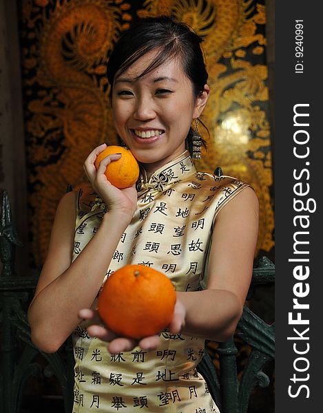 Beautiful Asian woman in cheongsam holding two oranges, suitable for Chinese New Year occasion. Beautiful Asian woman in cheongsam holding two oranges, suitable for Chinese New Year occasion.