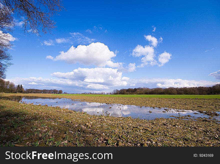 Farmland after the rain with puddle and blue sky and some clouds