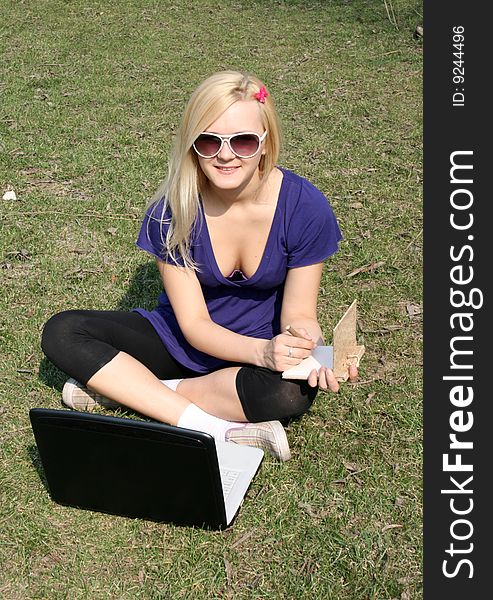 Smiling girl working on a laptop in a park