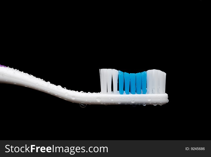 A horizontal closeup of a manual toothbrush with water droplets on a black background