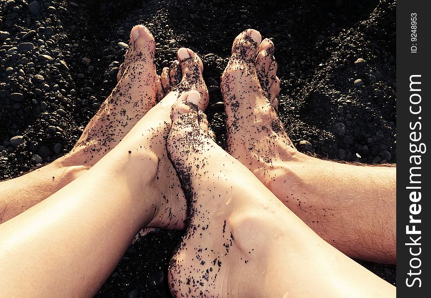 Feet in black sand on the beach