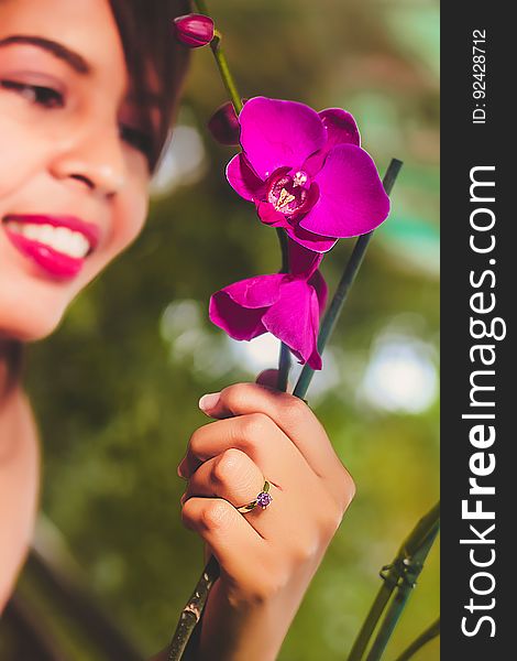 Smiling woman viewing her purple orchid flowers with selective focus on her ring and on the blooms. Smiling woman viewing her purple orchid flowers with selective focus on her ring and on the blooms.