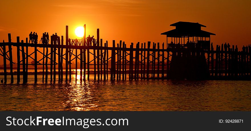 People walk on a pier at sunset.
