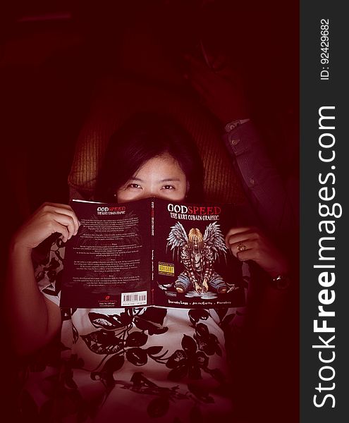 Young woman holding and reading a science fiction type book in the dark or at bedtime, dark background. Young woman holding and reading a science fiction type book in the dark or at bedtime, dark background.