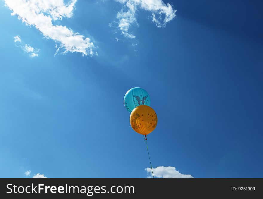 Two balloons shined with the sun through clouds against the sky