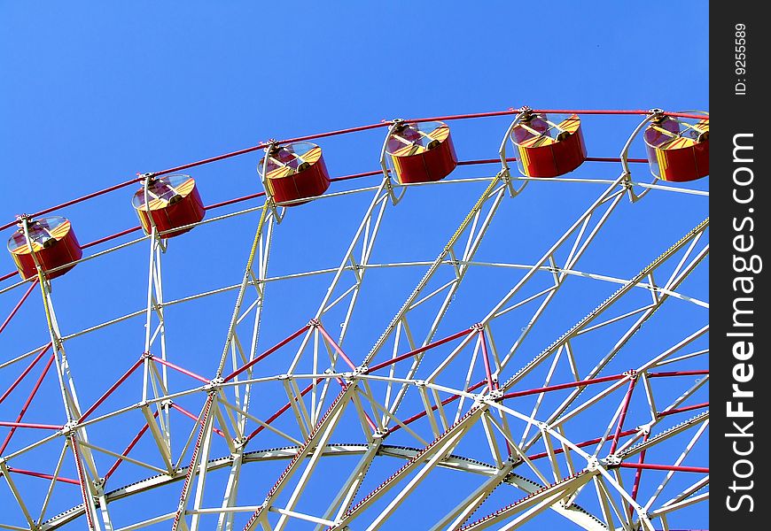 Big Ferris wheel with colored cabins on cloudy sky