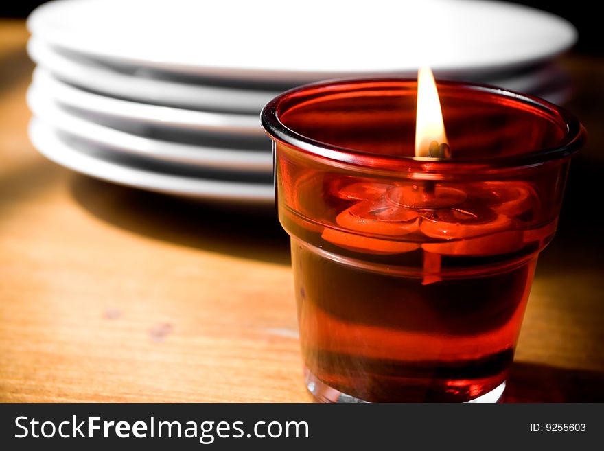 Portrait of a candle and stack of white plates set up on wooden table. focus on the candle flame. Portrait of a candle and stack of white plates set up on wooden table. focus on the candle flame.