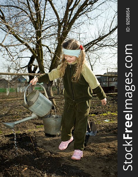 A pretty little girl watering soil  with a watering can in  her grandfather's  kitchen garden. A pretty little girl watering soil  with a watering can in  her grandfather's  kitchen garden