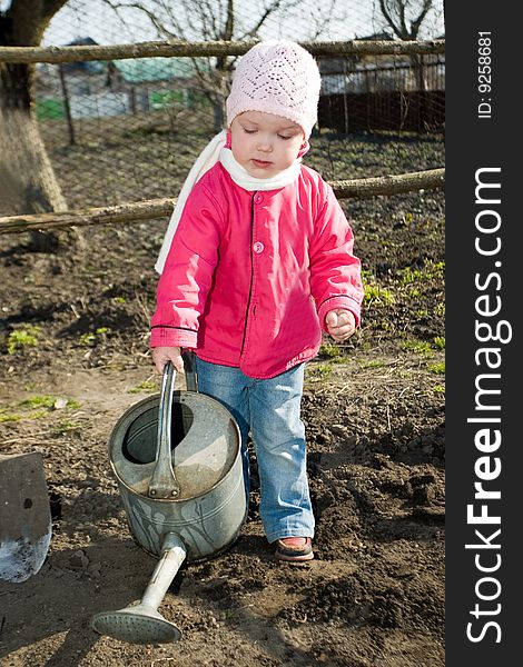 A pretty little girl watering soil  with a watering can in  her grandfather's  kitchen garden. A pretty little girl watering soil  with a watering can in  her grandfather's  kitchen garden