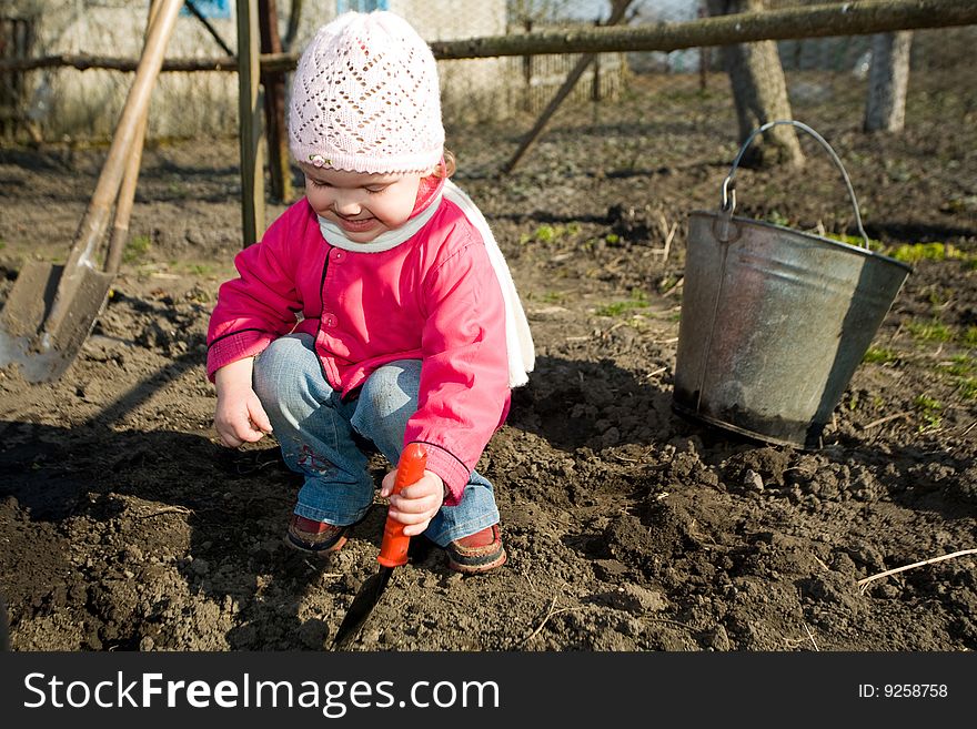 An  anxious little girl squatting down on the ground  cultivating soil  with  her  toy  spade. An  anxious little girl squatting down on the ground  cultivating soil  with  her  toy  spade
