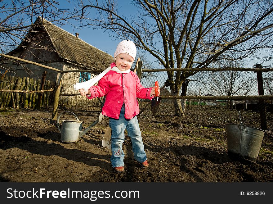 A smiling pretty little girl with a toy spade in hand in her grandfather's kitchen garden. A smiling pretty little girl with a toy spade in hand in her grandfather's kitchen garden