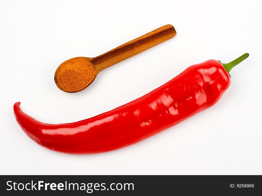 A pod of red pepper and a wooden spoonful of red ground pepper on a white background. A pod of red pepper and a wooden spoonful of red ground pepper on a white background