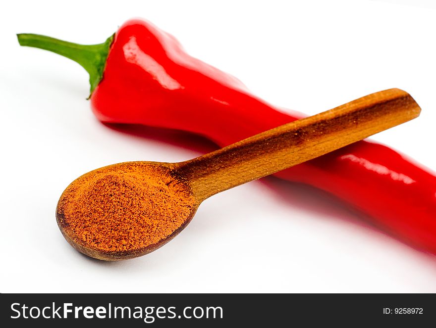 A composition of a wooden spoonful across a cut pod of red hot pepper on a white background. A composition of a wooden spoonful across a cut pod of red hot pepper on a white background