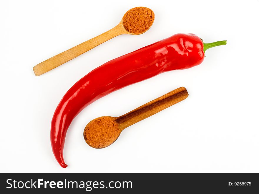 A composition of a pod of red chile pepper  and two wooden spoonful of red ground pepper on a white background. A composition of a pod of red chile pepper  and two wooden spoonful of red ground pepper on a white background