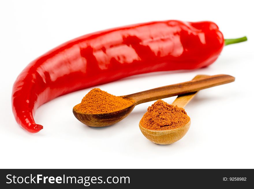 A composition of two intersected wooden spoonfull and a pod of red hot pepper on a white background. A composition of two intersected wooden spoonfull and a pod of red hot pepper on a white background