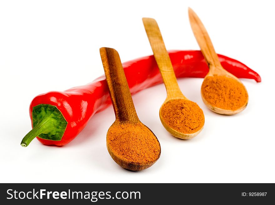 A composition of a pod of red Chile pepper and three wooden spoonful of ground red pepper on a white background. A composition of a pod of red Chile pepper and three wooden spoonful of ground red pepper on a white background